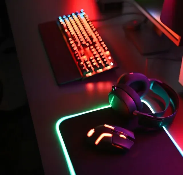 Escritorio oscuro con teclado, auriculares y ratón iluminados en rojo y verde